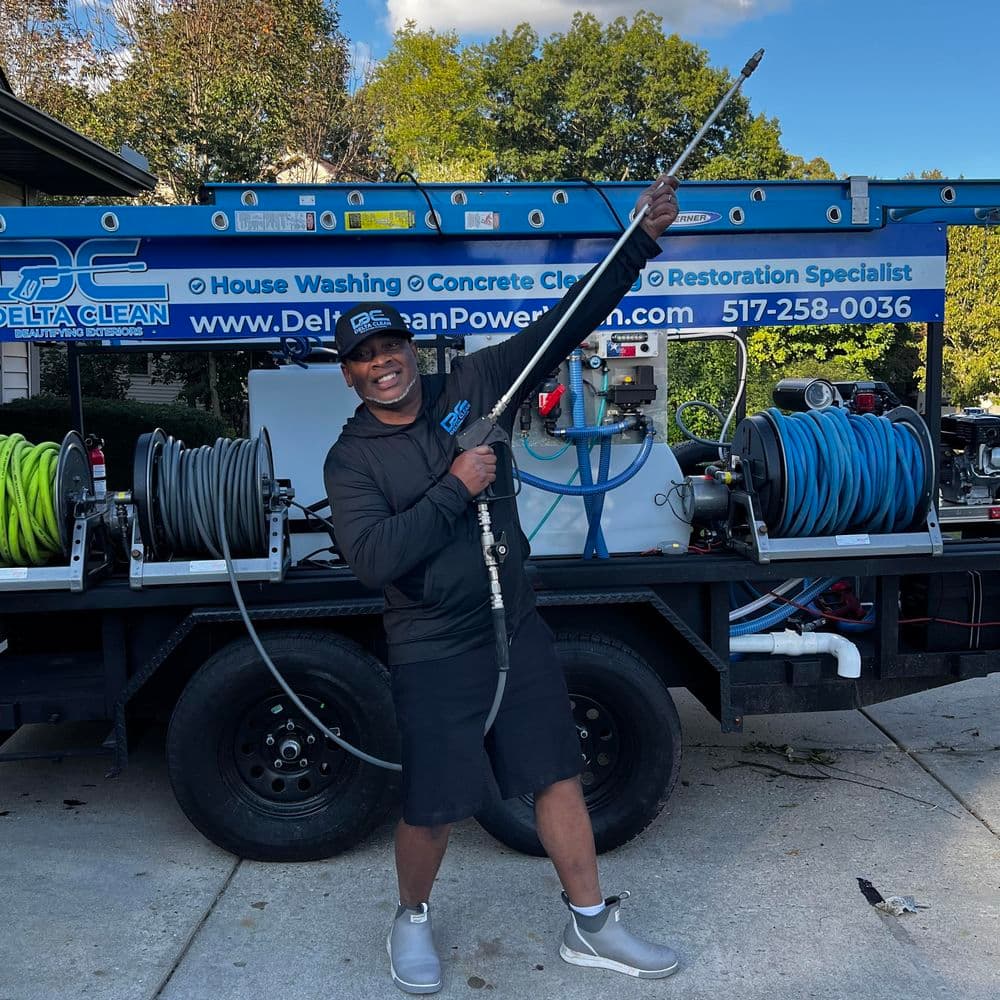 Man holding a pressure washer in front of a power washing truck with hoses and equipment.