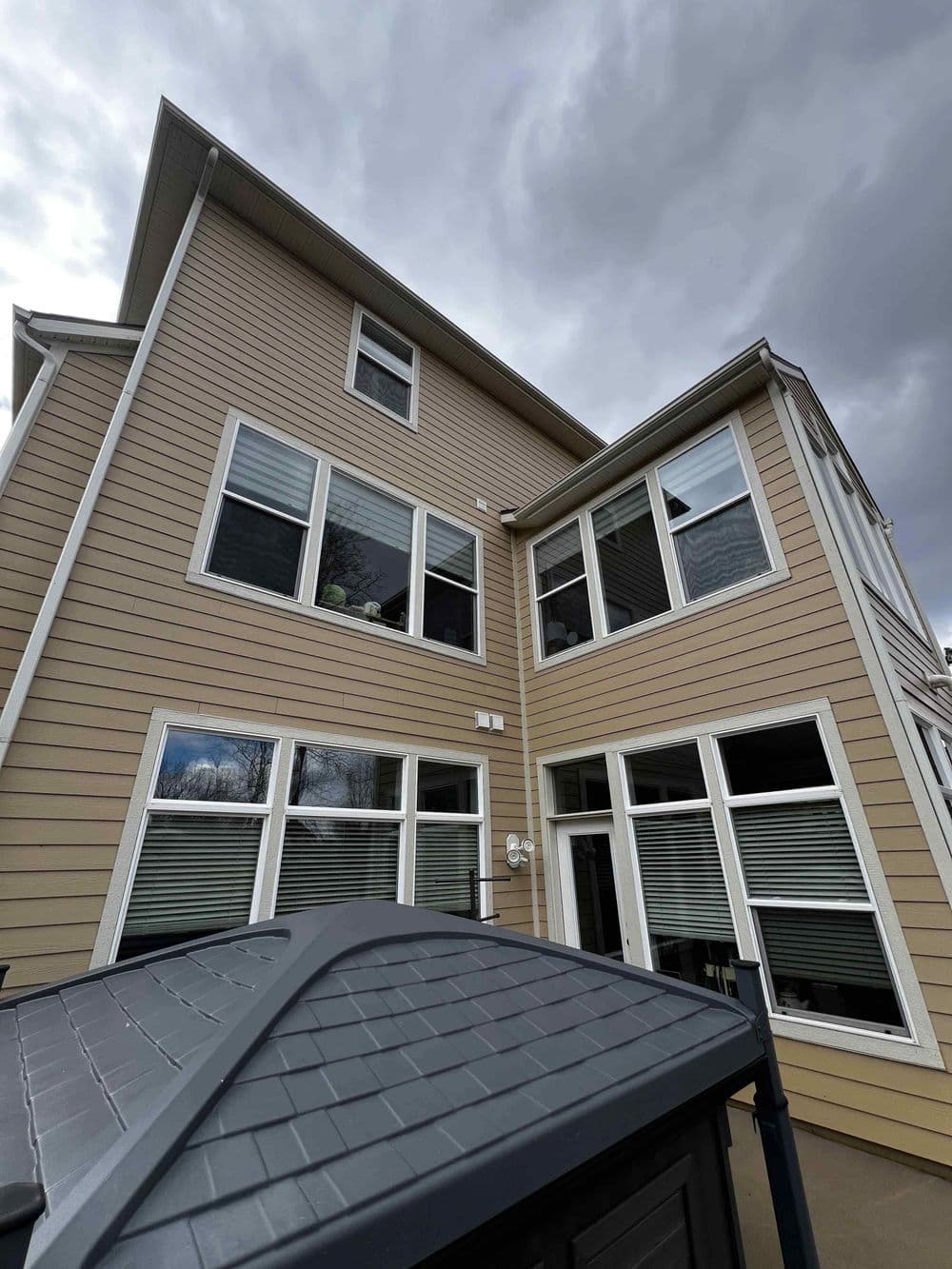 Modern two-story house with large windows and tan siding under a cloudy sky.